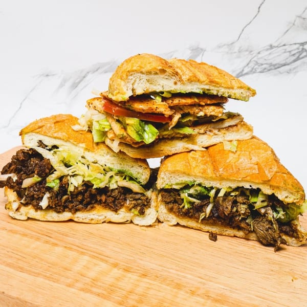 Three Mexican torta sandwiches on a wooden board, two with beef and one with chicken.