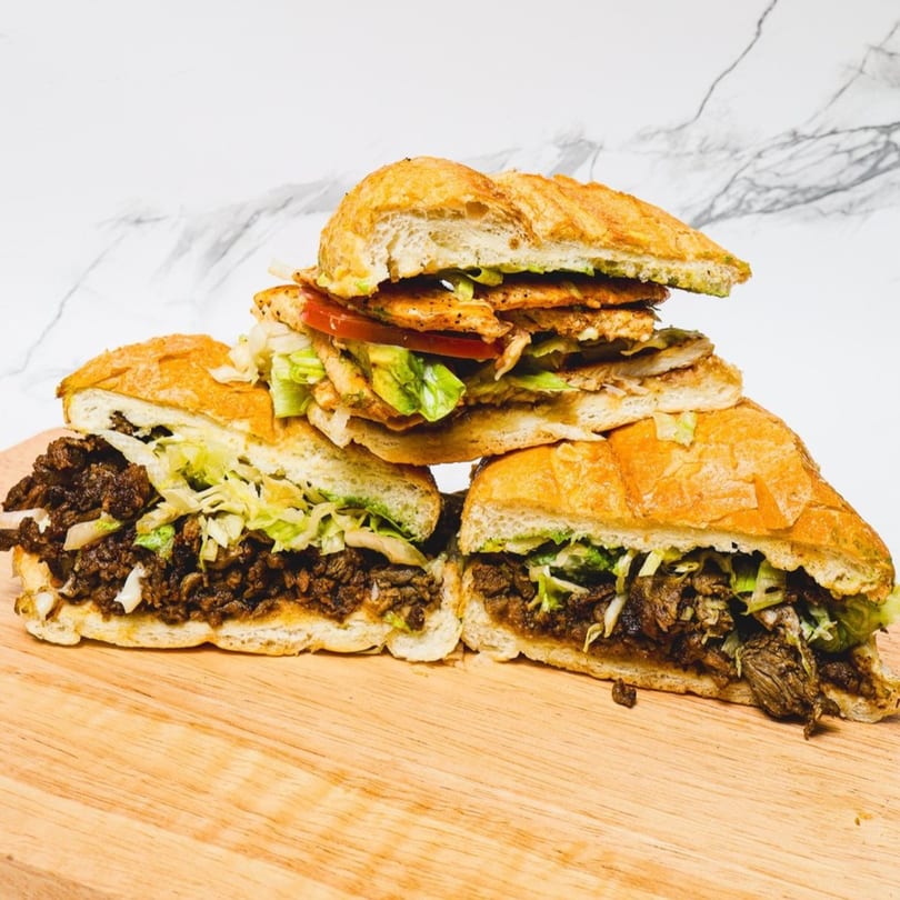 Three Mexican torta sandwiches on a wooden board, two with beef and one with chicken.